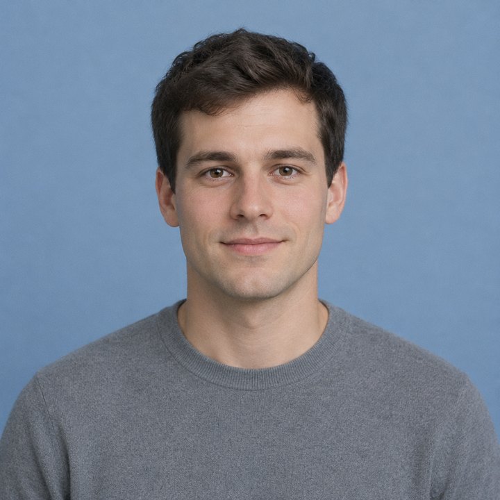 A man in a grey sweater in front of a blue studio backdrop